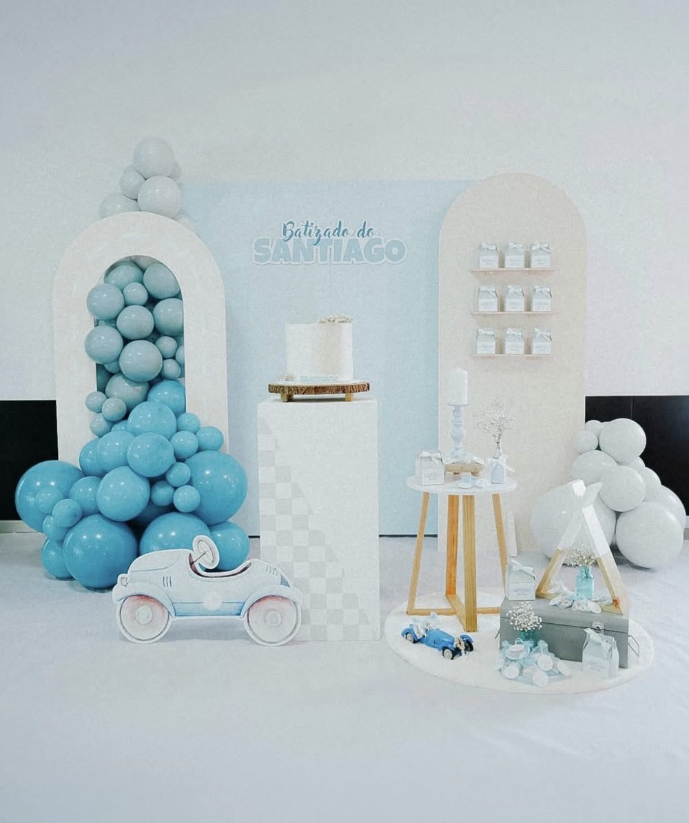 Decoração de batizado em tons de azul, com arcos, balões e a mesa do bolo